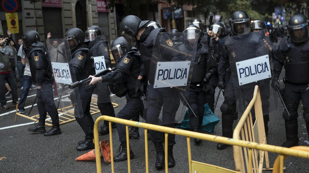 Einheiten der spanischen Nationalpolizei beseitigen Absperrungen, die man ihnen in den Weg geworfen hat, und einer zielt mit einem Gewehr für Gummigeschosse am 01.10.2017 in Barcelona (Spanien) vor einer zum Wahllokal für das Referendum bestimmten Schule.