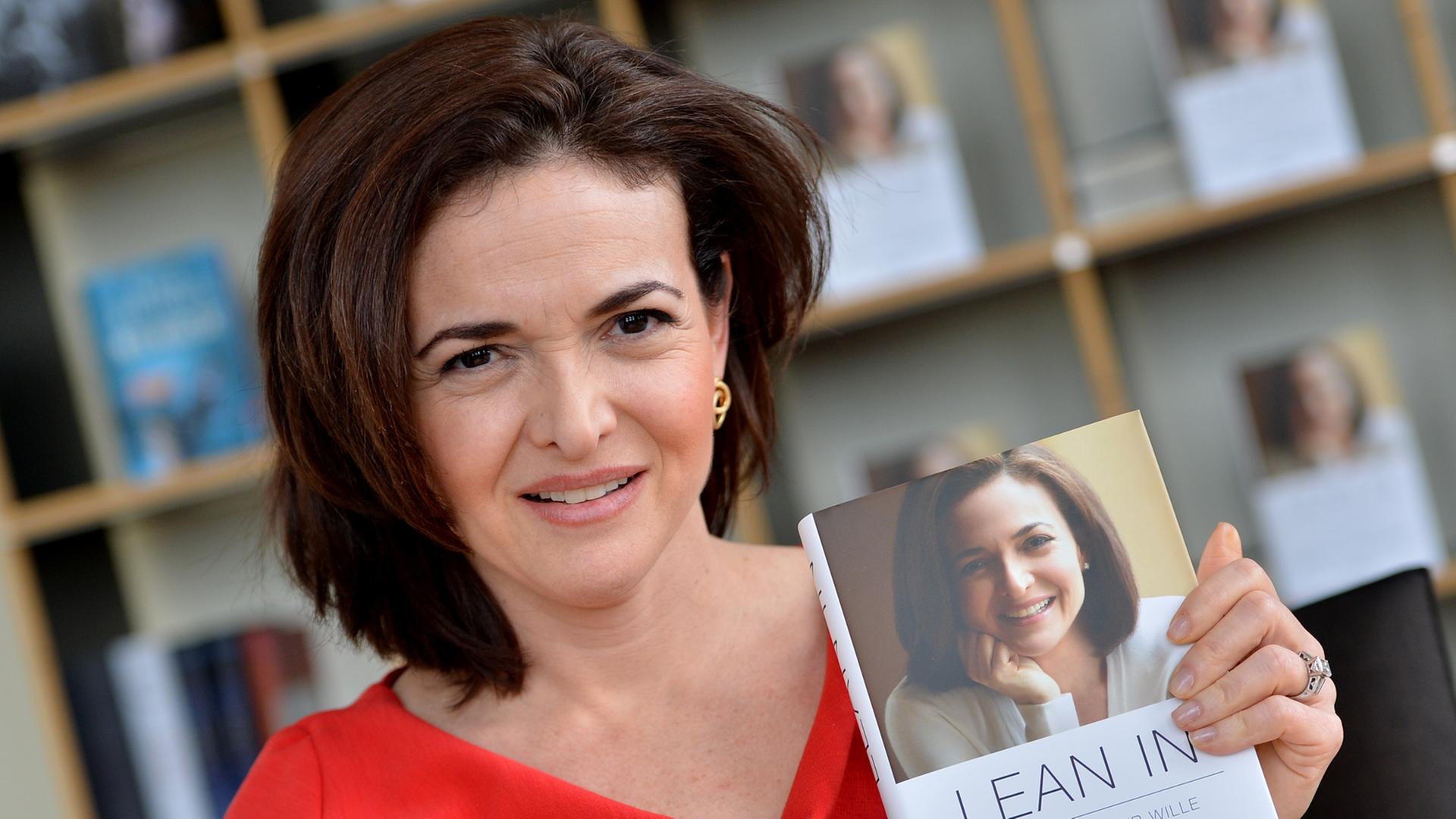 Sheryl Sandberg in rotem Kleid hält ein Buch mit dem Titel "Lean In" in die Kamera, auf dem Cover ist ihr Gesicht abgebildet. Sheryl Sandberg in rotem Kleid hält ein Buch mit dem Titel "Lean In" in die Kamera, auf dem Cover ist ihr Gesicht abgebildet.
