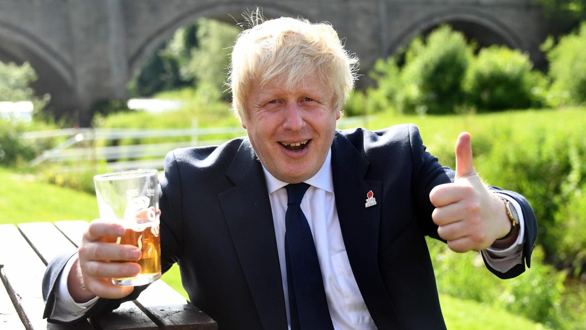 Der ehemalige Bürgermeister von London, Boris Johnson, sitzt während eines Auftritts für den EU-Austritt auf einer Bank. In einer Hand hält er ein Bier, bei der anderen Hand zeigt der Daumen nach oben.