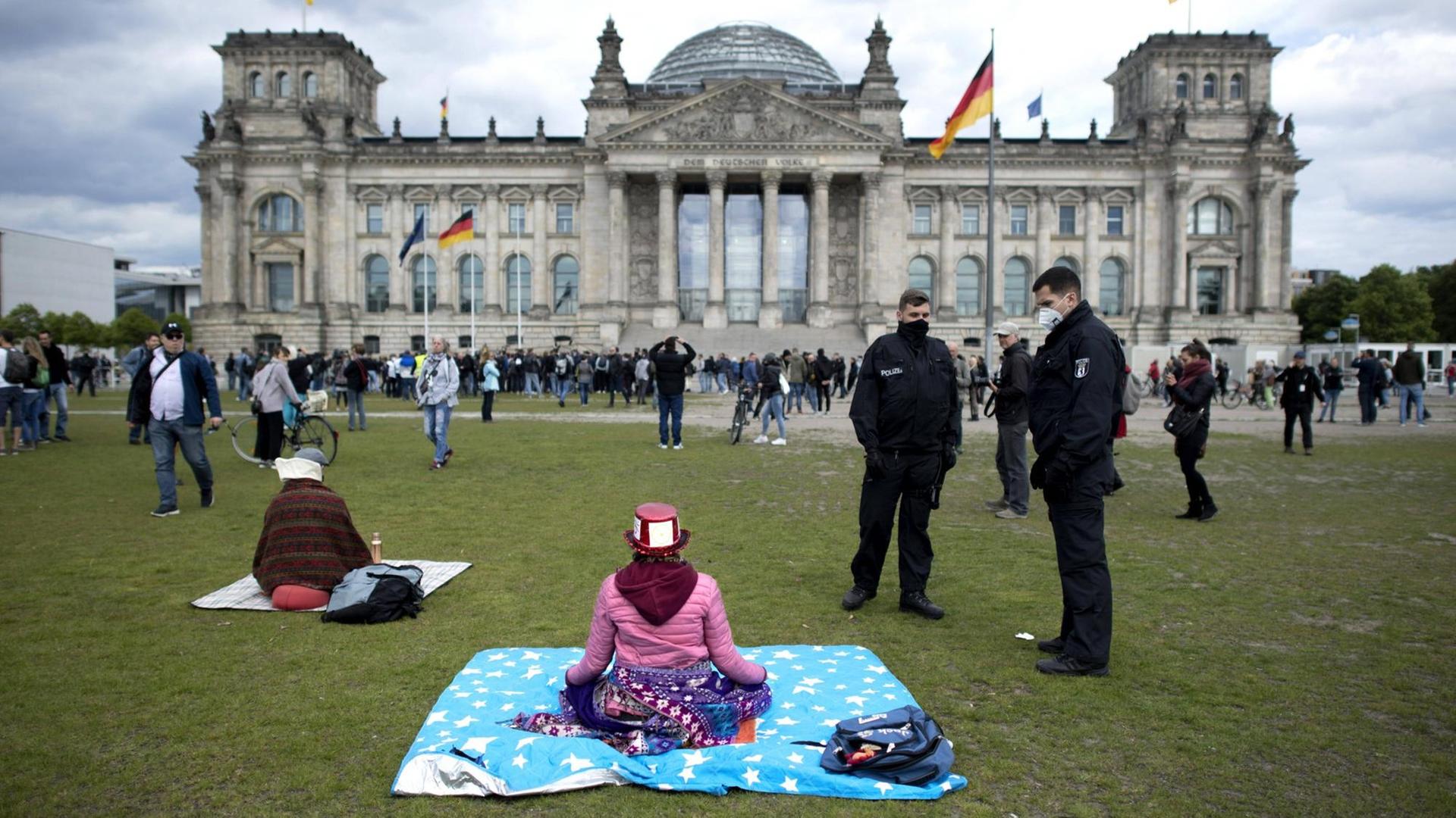 Polizisten fordern eine meditierende Frau während einer sogenannten Hygienedemo vor dem Reichstagsgebäude in Berlin auf, den Platz zu verlassen. Polizisten fordern eine meditierende Frau während einer sogenannten Hygienedemo vor dem Reichstagsgebäude in Berlin auf, den Platz zu verlassen.