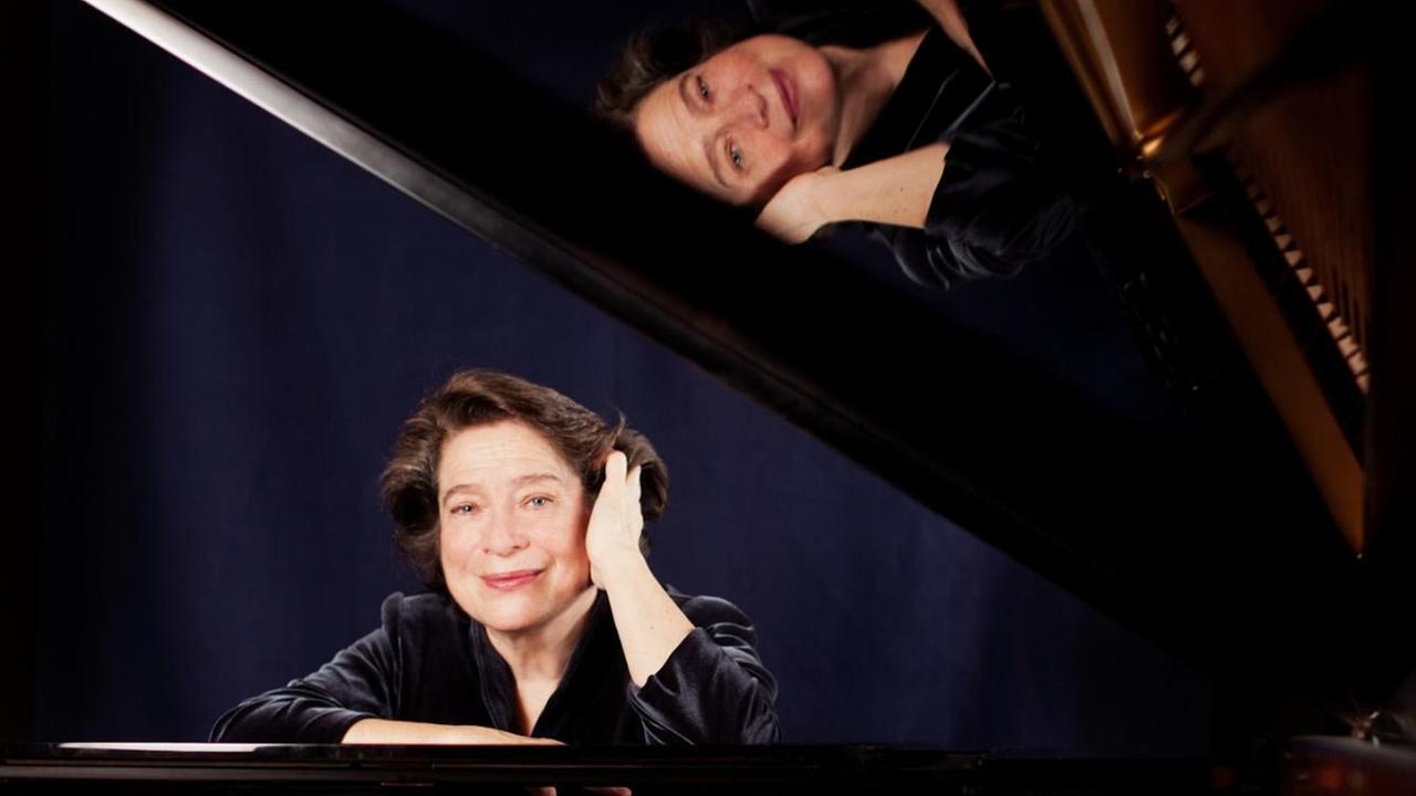 Eine Pianistin sitzt lächelnd am Flügel, wobbei sich ihr Gesicht im aufgeklappten Flügel widerspiegelt. Eine Pianistin sitzt lächelnd am Flügel, wobbei sich ihr Gesicht im aufgeklappten Flügel widerspiegelt.