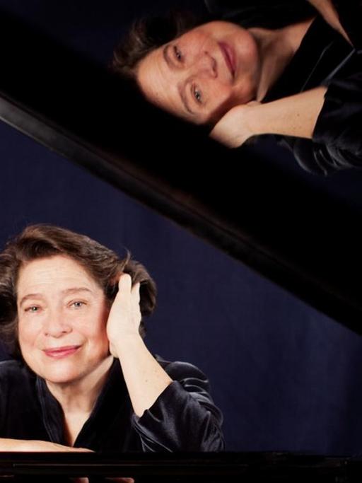 Eine Pianistin sitzt lächelnd am Flügel, wobbei sich ihr Gesicht im aufgeklappten Flügel widerspiegelt.