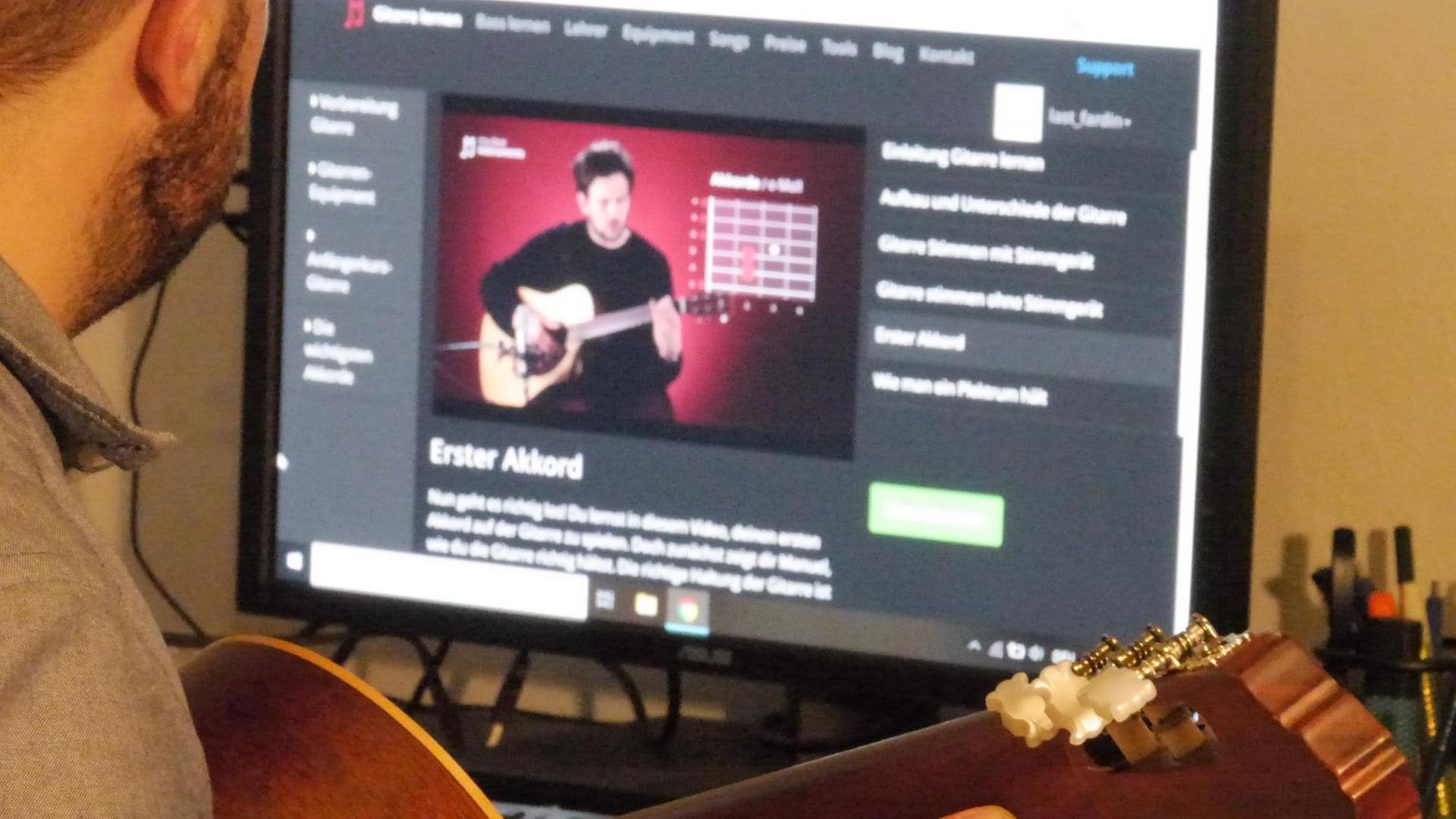 Overshoulder-Einstellung von Fardin Pfannkuche, der seine Gitarre hält und auf den Online-Videokurs auf seinem Laptop blickt. Overshoulder-Einstellung von Fardin Pfannkuche, der seine Gitarre hält und auf den Online-Videokurs auf seinem Laptop blickt.