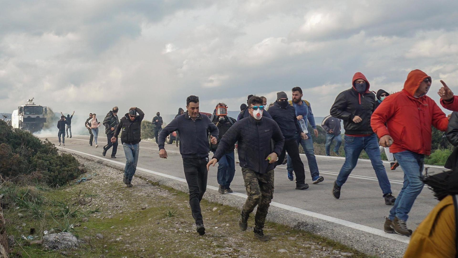 Demonstrierende rennen auf der Insel Lesobos eine Straße entlang, nachdem die Polizei Tränengas eingesetzt hat. Demonstrierende rennen auf der Insel Lesobos eine Straße entlang, nachdem die Polizei Tränengas eingesetzt hat.