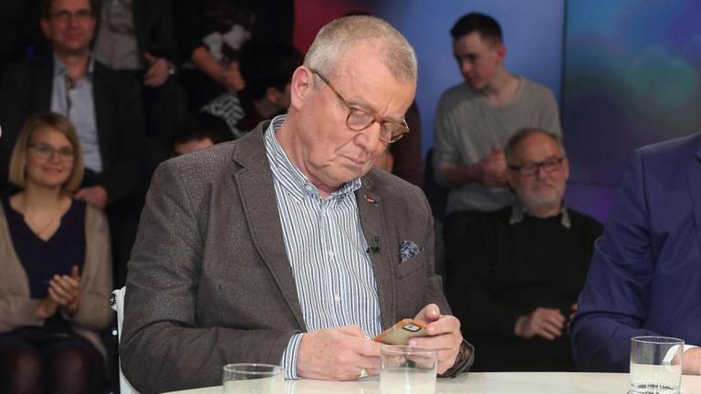 Der CDU-Politiker Ruprecht Polenz sitzt in einer Talkshow und schaut auf sein Mobiltelefon. Links und rechts neben ihm sitzen weitere Gäste.