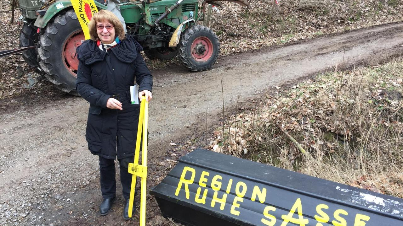 Anti-Atom-Aktivistin Heike Wiegel steht auf einem Waldweg, neben ihr ein schwarz gestrichener Sarg, auf dem steht "Region Asse, ruhe sanft", hinter ihr ein Traktor mit Anti-Atom-Flagge. Anti-Atom-Aktivistin Heike Wiegel steht auf einem Waldweg, neben ihr ein schwarz gestrichener Sarg, auf dem steht "Region Asse, ruhe sanft", hinter ihr ein Traktor mit Anti-Atom-Flagge.