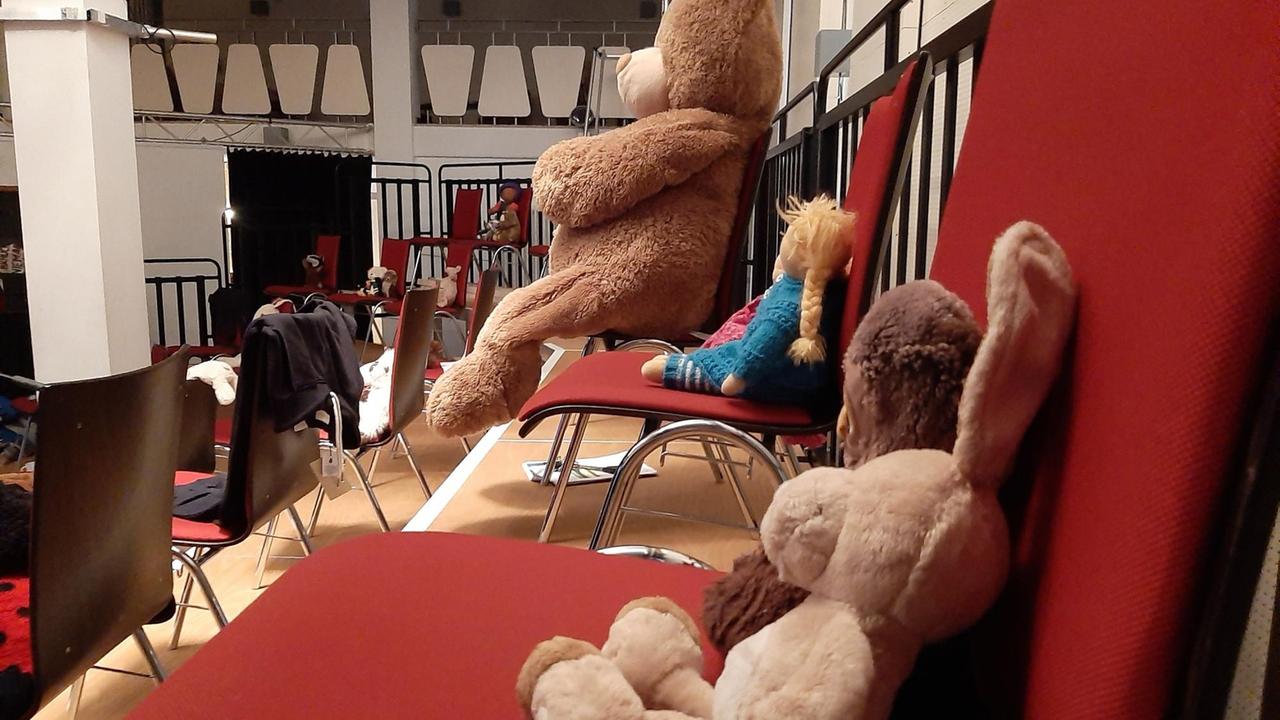 Auf den Publikumsplätzen (roten Stühlen) sitzen verschiende Kuscheltiere. Ein Plüschhase, ein menschengroßer Teddybär und eine Puppe. Auf den Publikumsplätzen (roten Stühlen) sitzen verschiende Kuscheltiere. Ein Plüschhase, ein menschengroßer Teddybär und eine Puppe.