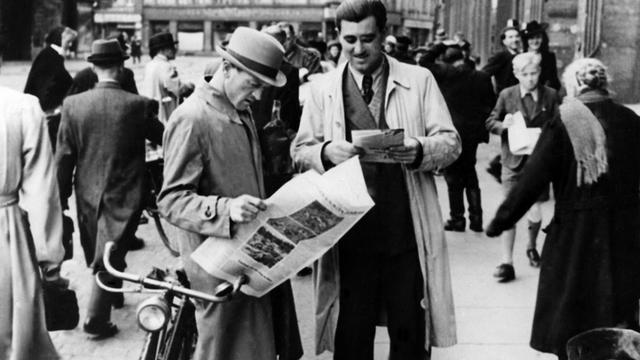 Das Bild zeigt zwei Männer, die die "Aachener Nachrichten" lesen, die als erste deutsche Zeitung nach dem Zweiten Weltkrieg erschien