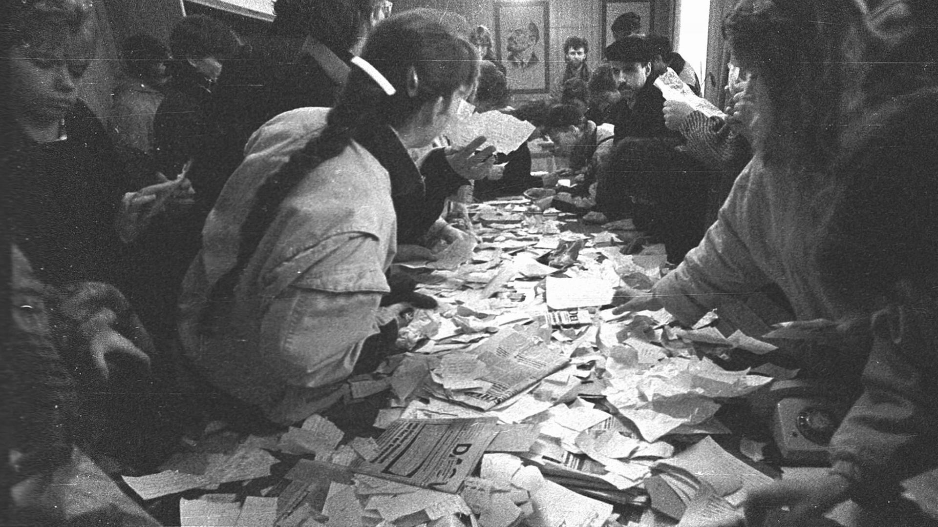 Menschen stehen am 4. Dezember 1989 in der Stasi-Zentrale in Erfurt in Thüringen um einen Tisch voll mit durchwühlten Unterlagen der Behörde. Menschen stehen am 4. Dezember 1989 in der Stasi-Zentrale in Erfurt in Thüringen um einen Tisch voll mit durchwühlten Unterlagen der Behörde.