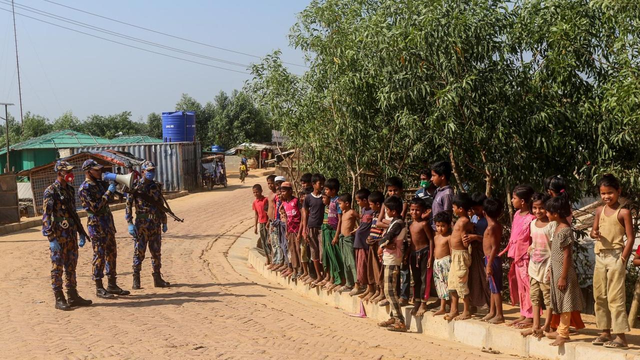 In this file photo taken on May 15, 2020 Security personnel (L) use a loudspeaker to raise awareness about the COVID-19 coronavirus in a Rohingya refugee camp in Ukhia. Four more Rohingya refugees at vast camps in Bangladesh have tested positive for coronavirus, taking the total to 25, health officials said on May 25, 10 days after the first cases were confirmed. Health experts have long feared that the virus could spread quickly through the crowded settlements