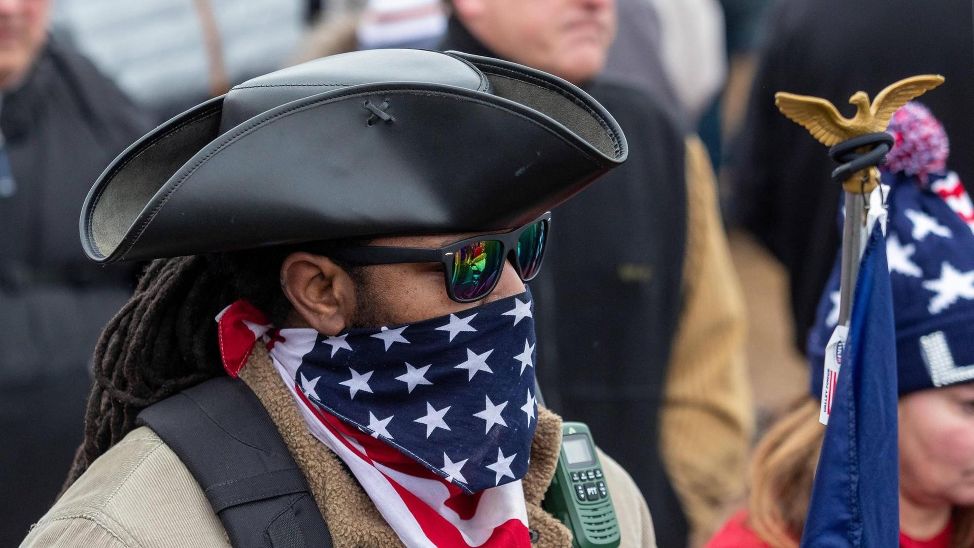 Pro-Trump-Demonstrant mit Sonnenbrille, Cowboyhut und vor den Mund gebundenem Tuch mit dem Motiv der US-Nationalflagge.