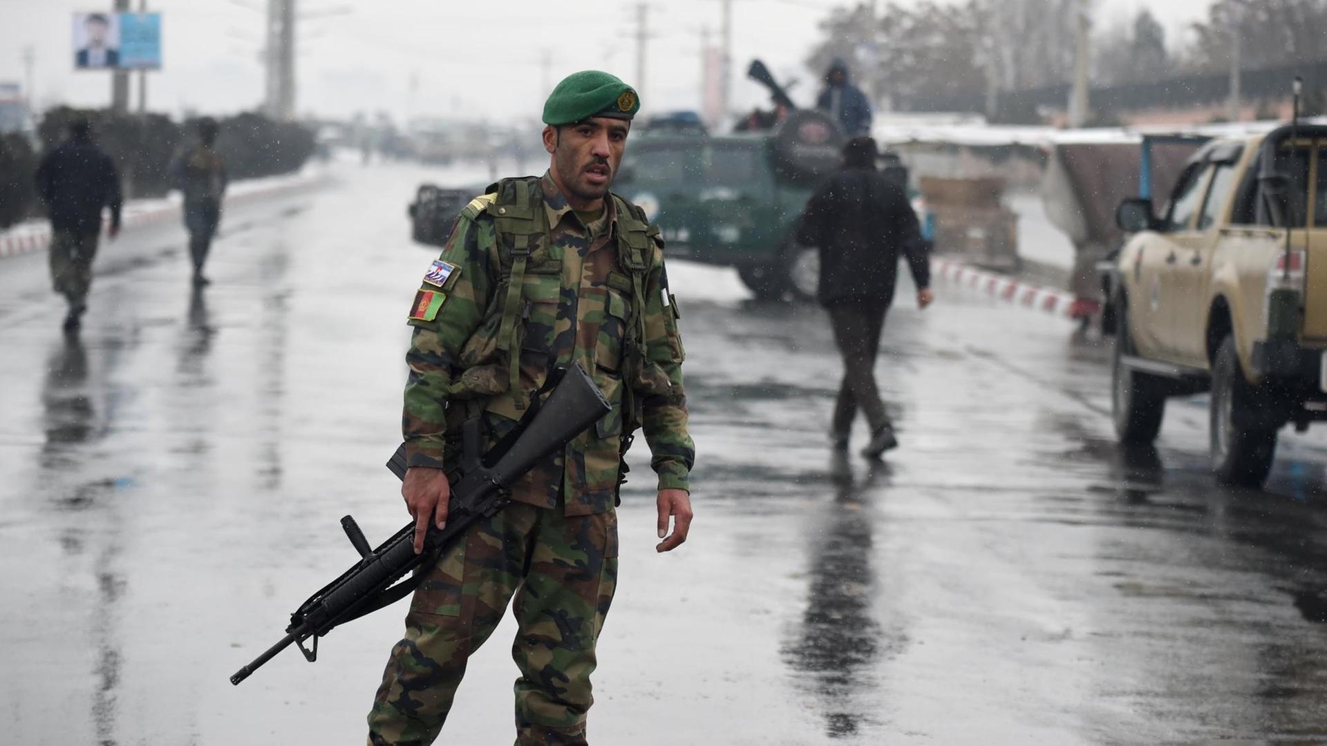 Ein uniformierter Soldat mit Maschinengewehr läuft über die Straße, im Hintergrund weitere Soldaten und Militärfahrzeuge. Ein uniformierter Soldat mit Maschinengewehr läuft über die Straße, im Hintergrund weitere Soldaten und Militärfahrzeuge.