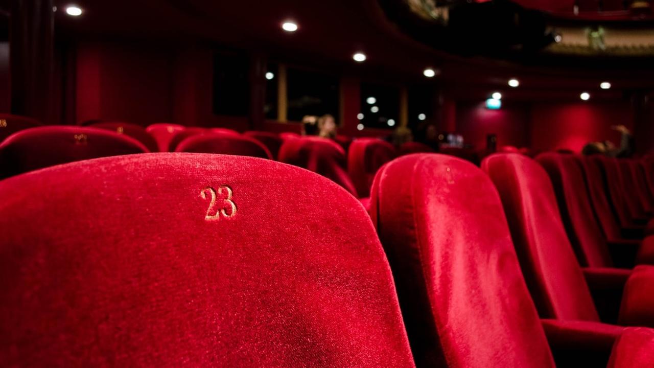 Das Foto zeigt in Großaufnahme leere rotsamtene Sitze in der Sitzreihe eines Theatersaal. Ein Sitz trägt die Nummer 23. Das Foto zeigt in Großaufnahme leere rotsamtene Sitze in der Sitzreihe eines Theatersaal. Ein Sitz trägt die Nummer 23.