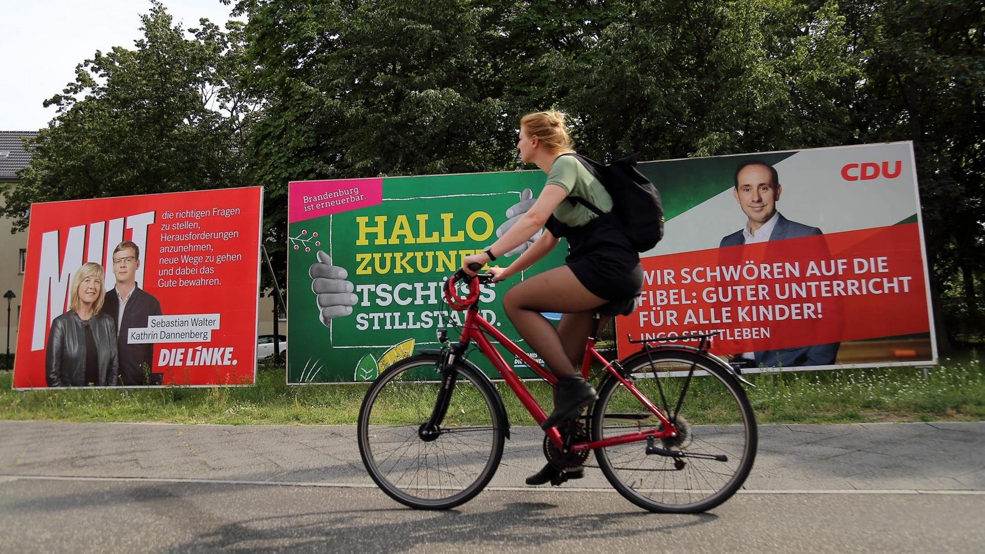 Fahrradfahrerin vor Wahlplakaten von Die Linke, Bündnis 90/Die Grünen und CDU für die Landtagswahl in Brandenburg