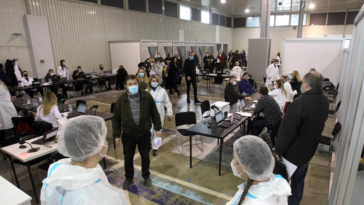 In den Belgrader Messehallen sind Kabinen für Corona-Impfungen aufgebaut. Außerdem Tische zur Registrierung der Impflinge. Vor den Kabinen warten Menschen mit Mund-Nasen-Schutz. In den Belgrader Messehallen sind Kabinen für Corona-Impfungen aufgebaut. Außerdem Tische zur Registrierung der Impflinge. Vor den Kabinen warten Menschen mit Mund-Nasen-Schutz.