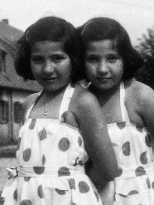 Zwillingsmädchen mit gepunkteten Sommerkleidern stehen auf eine der Straßenzüge in Föhrenwald.