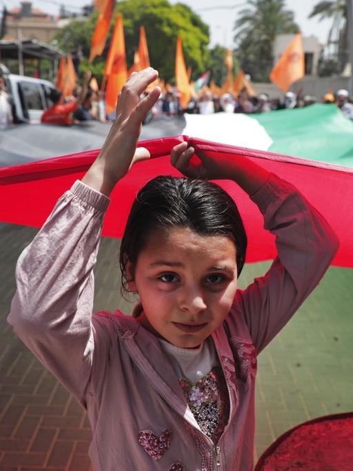 Ein kleines Mädchen läuft vorneweg und hält mit vielen anderen die palästinensische Flagge hoch.