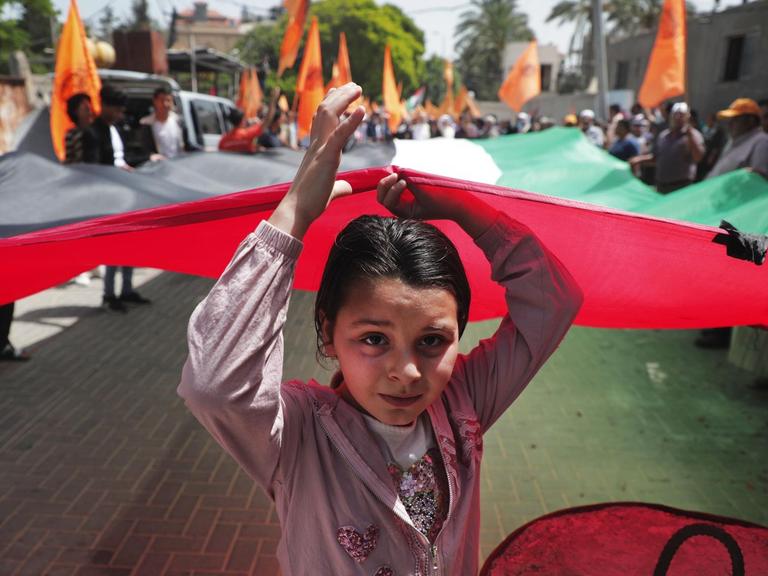 Ein kleines Mädchen läuft vorneweg und hält mit vielen anderen die palästinensische Flagge hoch.