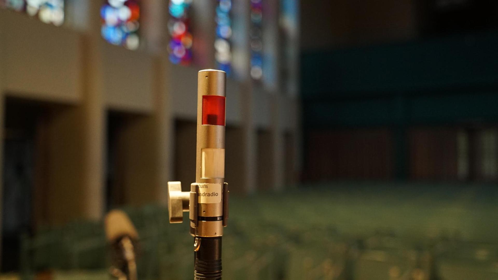 Eine schmale Rotlichtlampe steht inmitten eines Kirchenraumes.