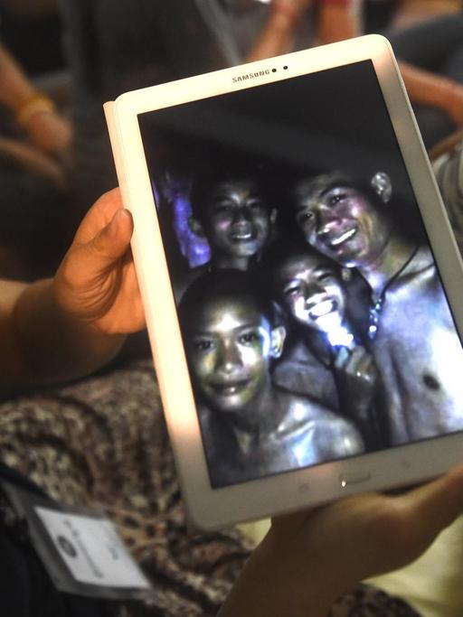 Ein Familienmitglied zeigt ein Bild von Kindern aus einer Jugendfußballmannschaft, die tagelang in einer Höhle in Thailand eingeschlossen waren.