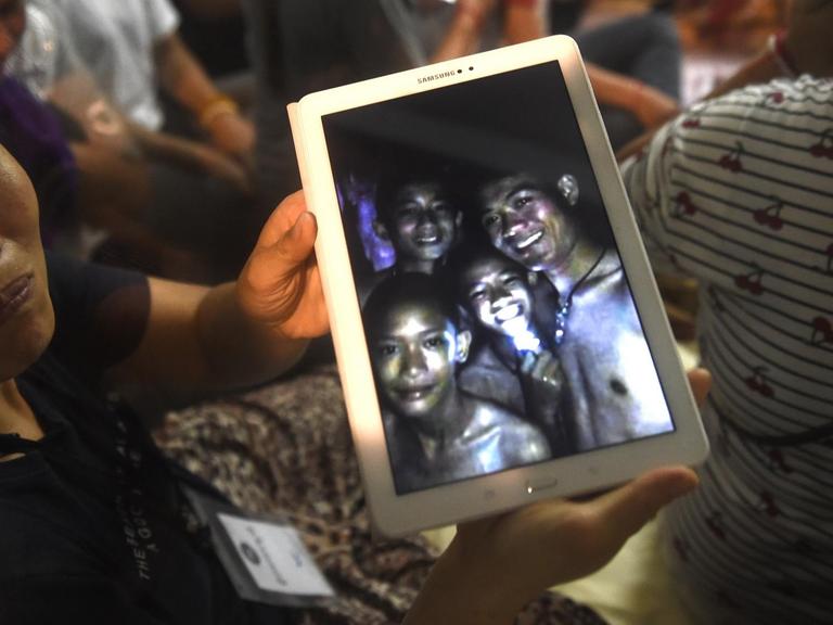 Ein Familienmitglied zeigt ein Bild von Kindern aus einer Jugendfußballmannschaft, die tagelang in einer Höhle in Thailand eingeschlossen waren.
