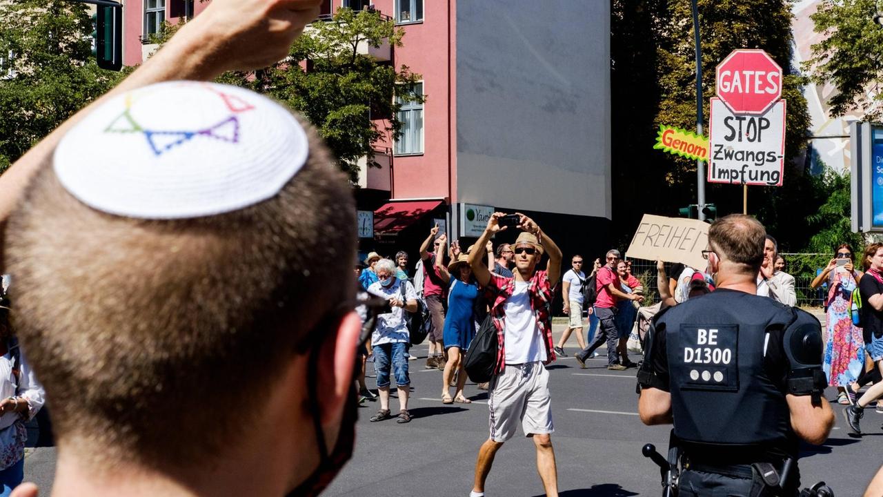 Ein Mann mit Kippa und Mundschutz blickt auf eine Demonstration von Impfgegnern in Berlin Ein Mann mit Kippa und Mundschutz blickt auf eine Demonstration von Impfgegnern in Berlin