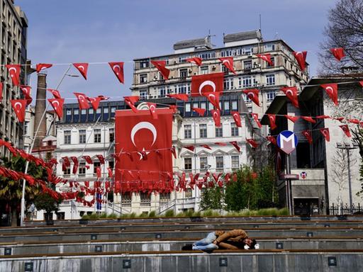 Zahlreiche leere Bänke unter vielen rot-weißen kleinen türkischen Flaggen in Istanbul. Auf einer der Bänke ganz vorne schläft ein Obdachloser.