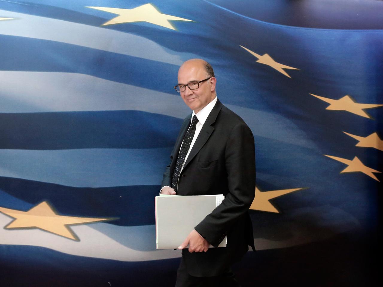 Frankreichs ehemaliger Finanzminister und Kandidat für die EU-Kommission Pierre Moscovici, geht vor einer großen blauen EU-Flagge mit gelben Sternen und weißen Streifen entlang Frankreichs ehemaliger Finanzminister und Kandidat für die EU-Kommission Pierre Moscovici, geht vor einer großen blauen EU-Flagge mit gelben Sternen und weißen Streifen entlang