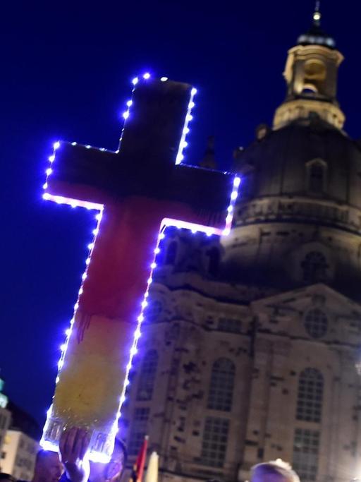 Ein Anhänger der PEGIDA-Bewegung hält auf der Protestkundgebung vor der Frauenkirche in Dresden ein in deutschen Nationalfarben gemaltes Kreuz in der Hand.