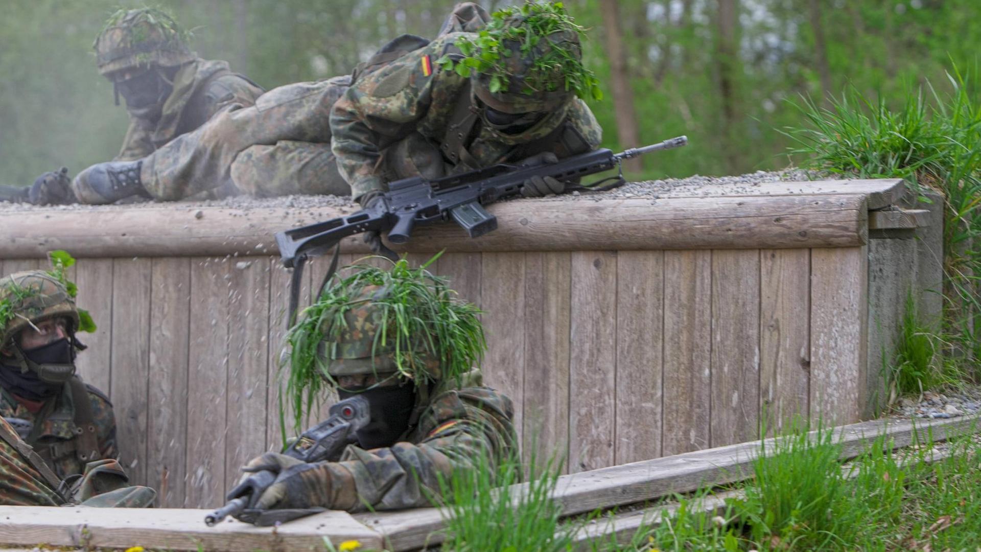 Bewaffnete Soldaten der Bundeswehr in Tarnuniform überwinden ein Hindernis bei einer Übung. Bewaffnete Soldaten der Bundeswehr in Tarnuniform überwinden ein Hindernis bei einer Übung.