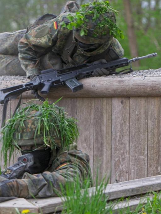 Bewaffnete Soldaten der Bundeswehr in Tarnuniform überwinden ein Hindernis bei einer Übung.