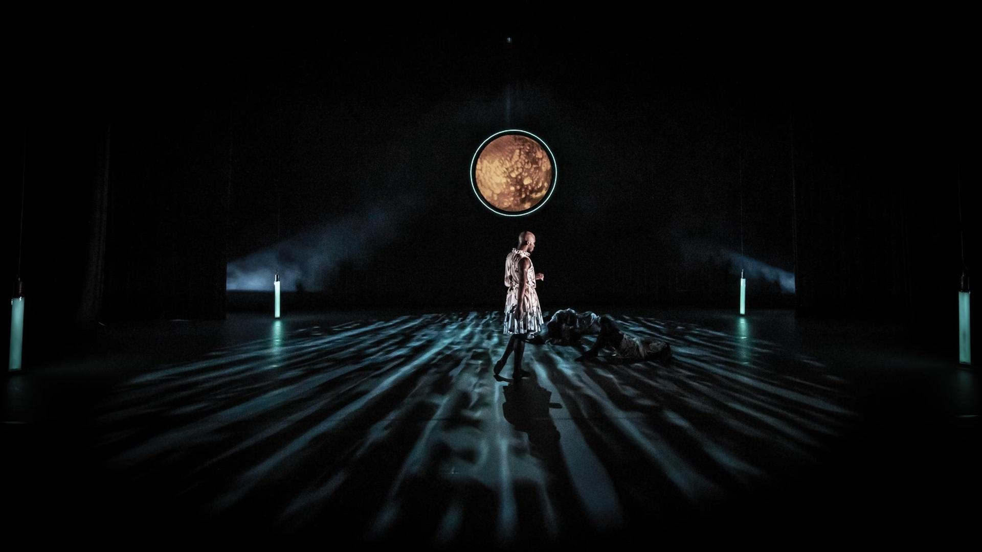 Szene aus dem Requiem: Ein Mann in einem Kleid steht auf einer mondbeschienenen Bühne. Am Boden liegen Tänzer.