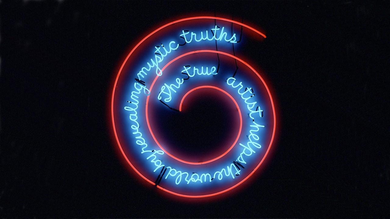 Eine blaue Leuchtschrift zeigt den verschnörkelten Schriftzug: "The true artist helps the world by revealing mystic truths."