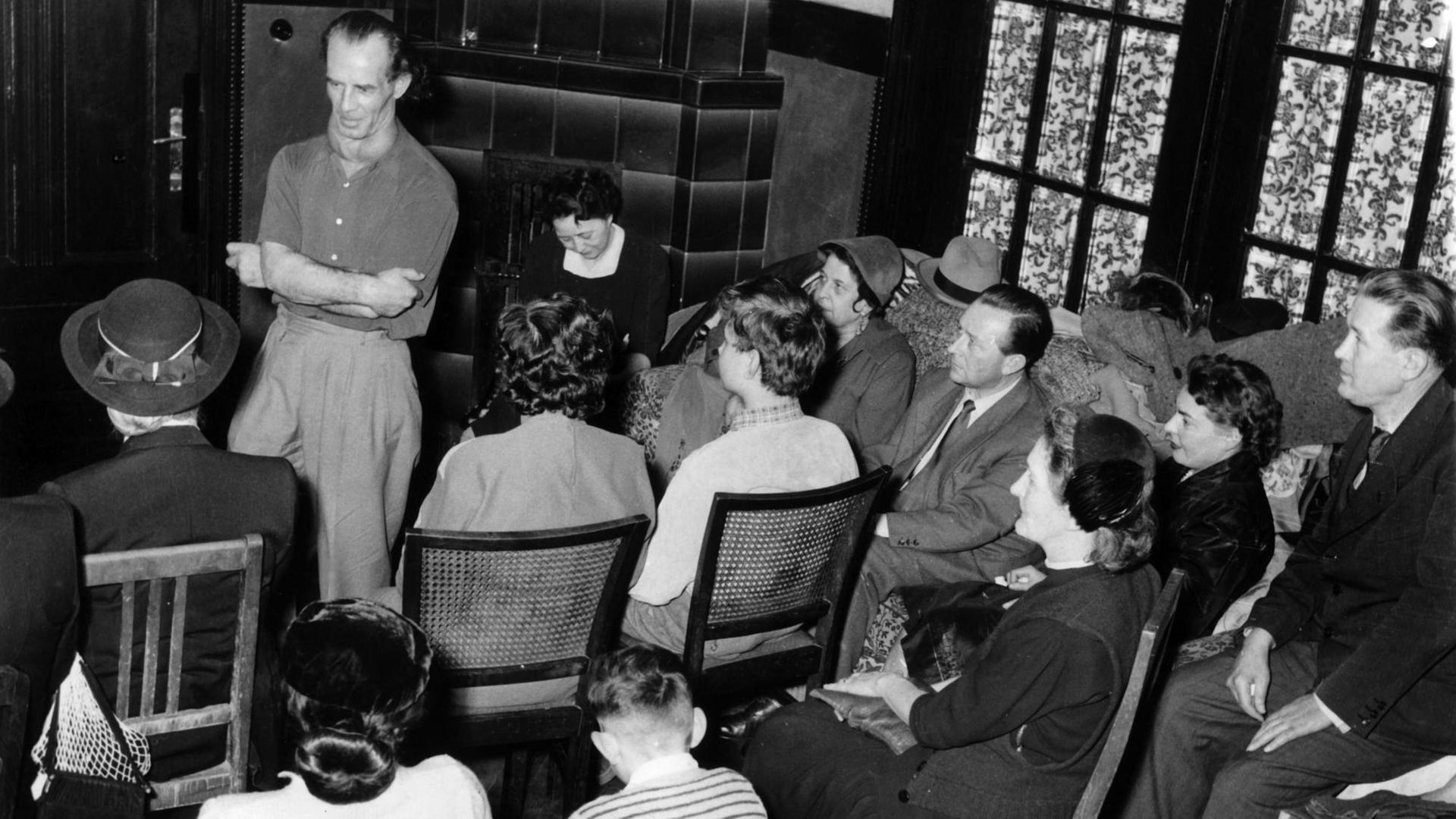 "Wunderheiler" Bruno Gröning (l, stehend) spricht 1955 in Düsseldorf in einer Privatversammlung vor geladenen Gästen.