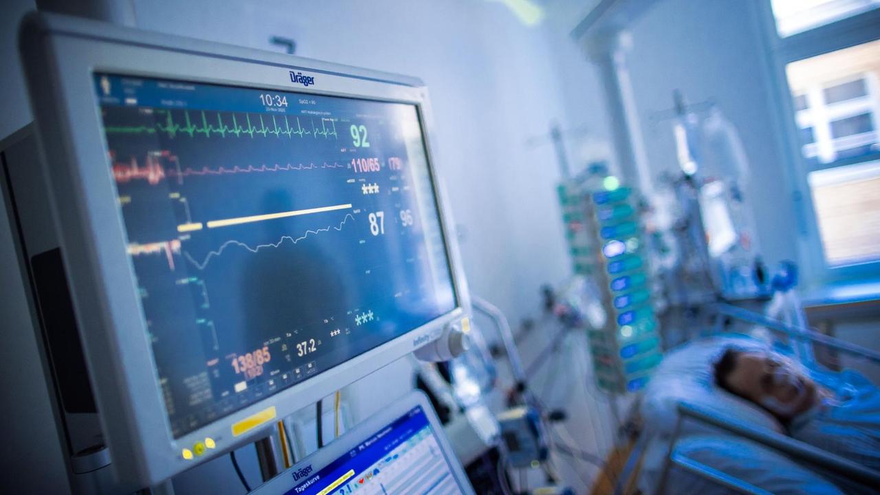 Hinter Überwachungsmonitoren liegt ein Corona-Patient in einem Raum einer Intensivstation. Hinter Überwachungsmonitoren liegt ein Corona-Patient in einem Raum einer Intensivstation.