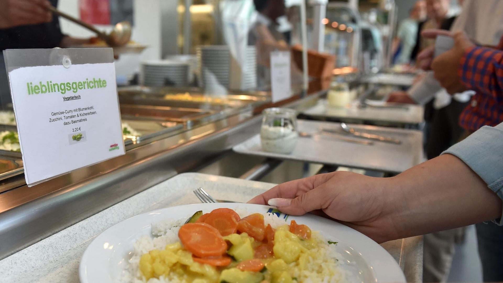 Zwei Hände stellen einen Teller Essen auf ein Tablett in einer Kantine. Zwei Hände stellen einen Teller Essen auf ein Tablett in einer Kantine.