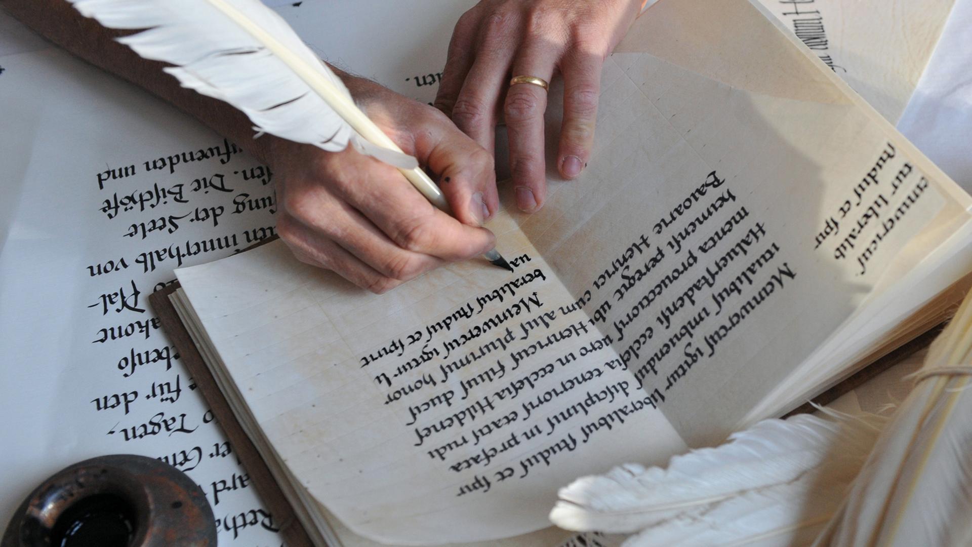 Eine Hand schreibt mit einer Schreibfeder in altertümlicher Schrift in ein Heft. Eine Hand schreibt mit einer Schreibfeder in altertümlicher Schrift in ein Heft.