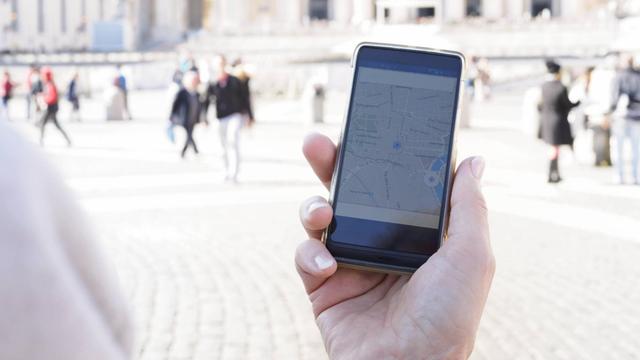 Eine Frau hält ein Smartphone mit der eingeschalteten GPS Funktion in der Hand. Sie befindet sich in Rom