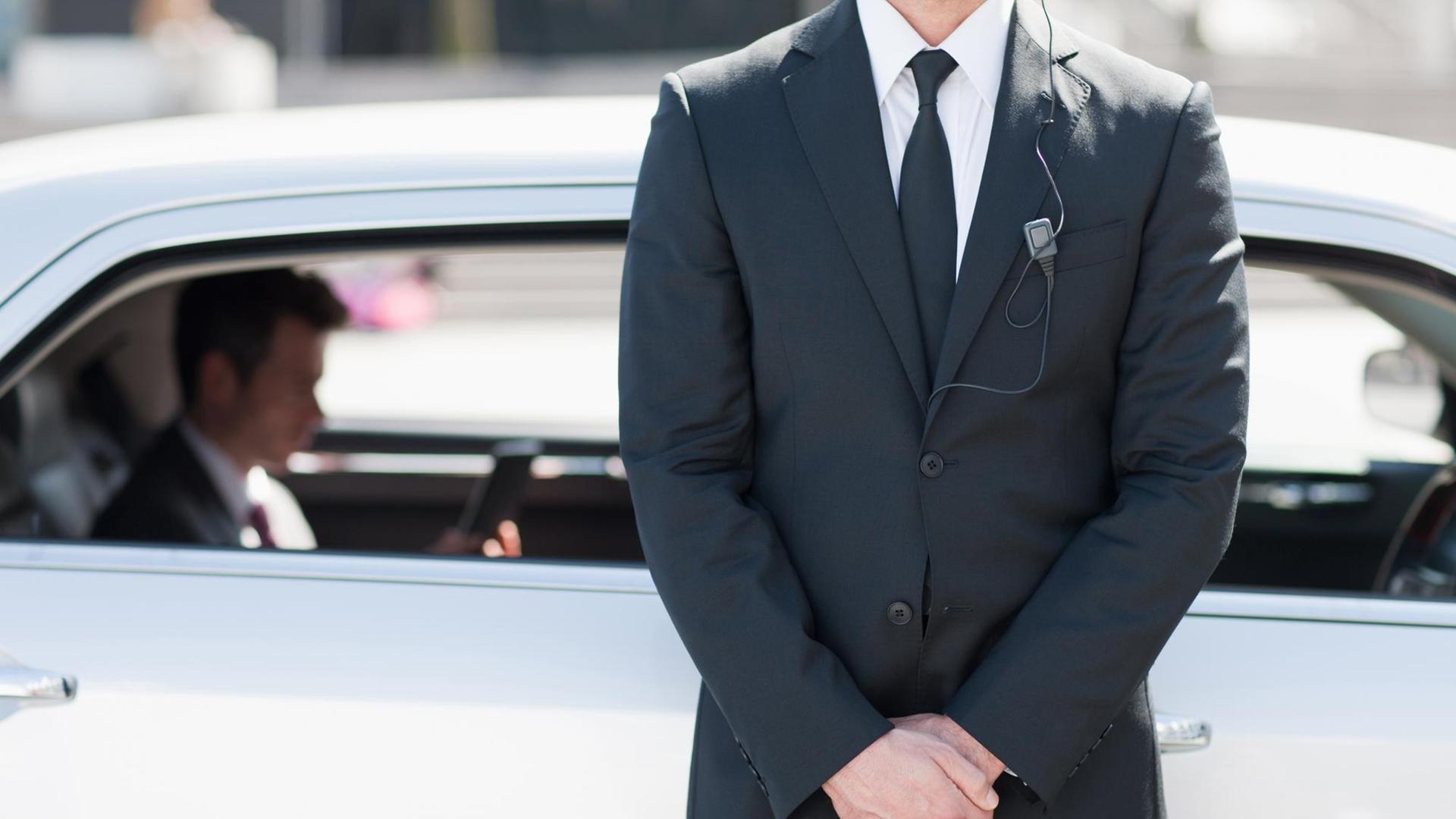 Ein Securitymann im Anzug steht vor einem gepanzertem Auto. (Symbolbild) Ein Securitymann im Anzug steht vor einem gepanzertem Auto. (Symbolbild)