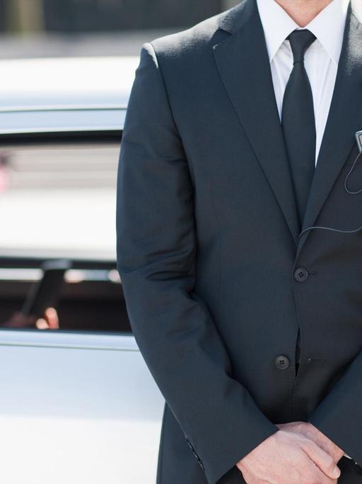 Ein Securitymann im Anzug steht vor einem gepanzertem Auto. (Symbolbild)
