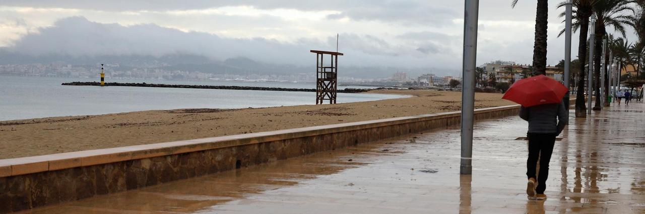 Ein Mann spaziert mit einem Regenschirm am Strand von Palma entlang. Ein Mann spaziert mit einem Regenschirm am Strand von Palma entlang.