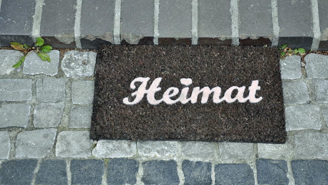 Ein Fußabtreter mit dem Schriftzug "Heimat"liegt auf einem gepflasterten Weg. Ein Fußabtreter mit dem Schriftzug "Heimat"liegt auf einem gepflasterten Weg.