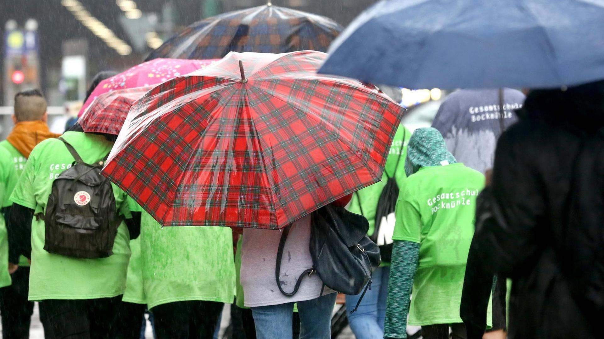 Menschen stehen mit Schirmen in einem Regenschauer.