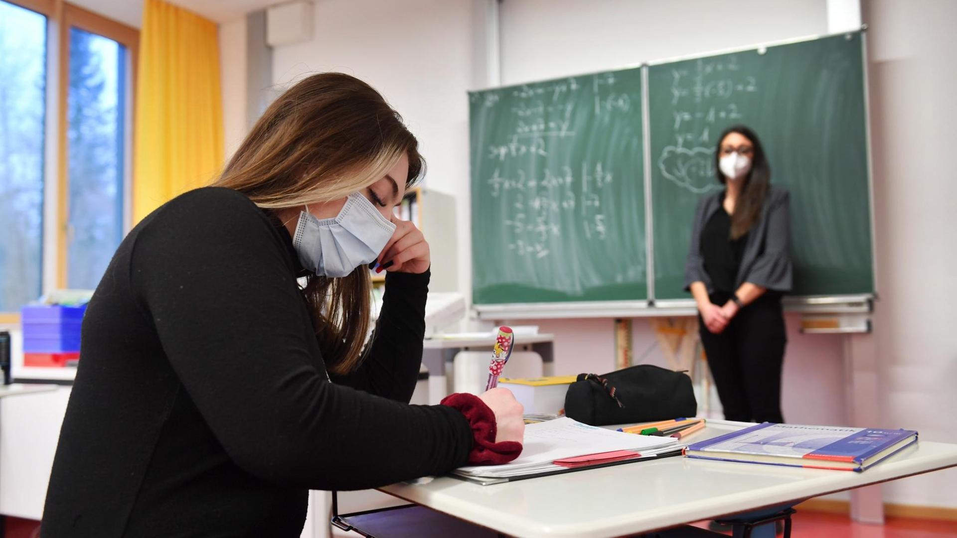 Eine Schülerin sitzt in einem Klassen-Zimmer. Die Lehrerin steht an der Tafel. Eine Schülerin sitzt in einem Klassen-Zimmer. Die Lehrerin steht an der Tafel.