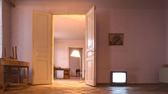 Eine halb leergeräumte Altbauwohnung, Möbel stehen in der Ecke und ein Fernseher leuchtet auf dem Fussboden.