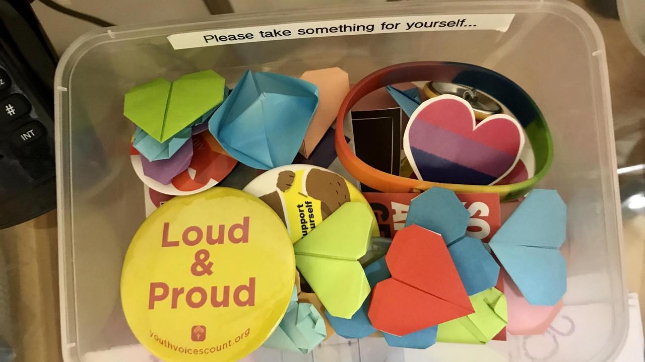 Bunte Papier- und Plastiksticker durcheinandergeworfen in einer Kiste. Auf einem großen runden gelben Sticker steht "Loud & Proud". Bunte Papier- und Plastiksticker durcheinandergeworfen in einer Kiste. Auf einem großen runden gelben Sticker steht "Loud & Proud".