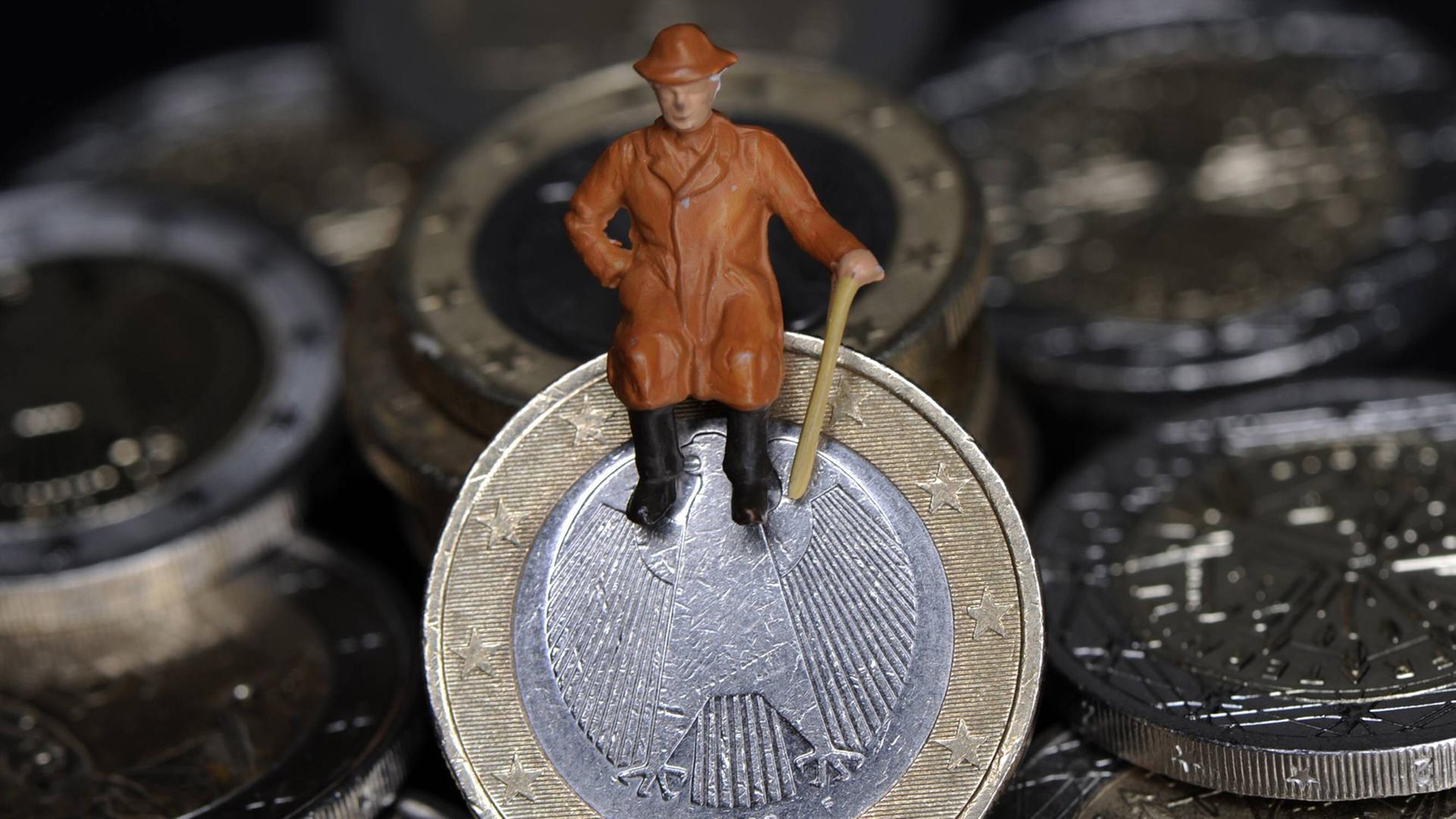 Eine Figur eines älteren Mannes sitzt auf einer Euro-Münze.