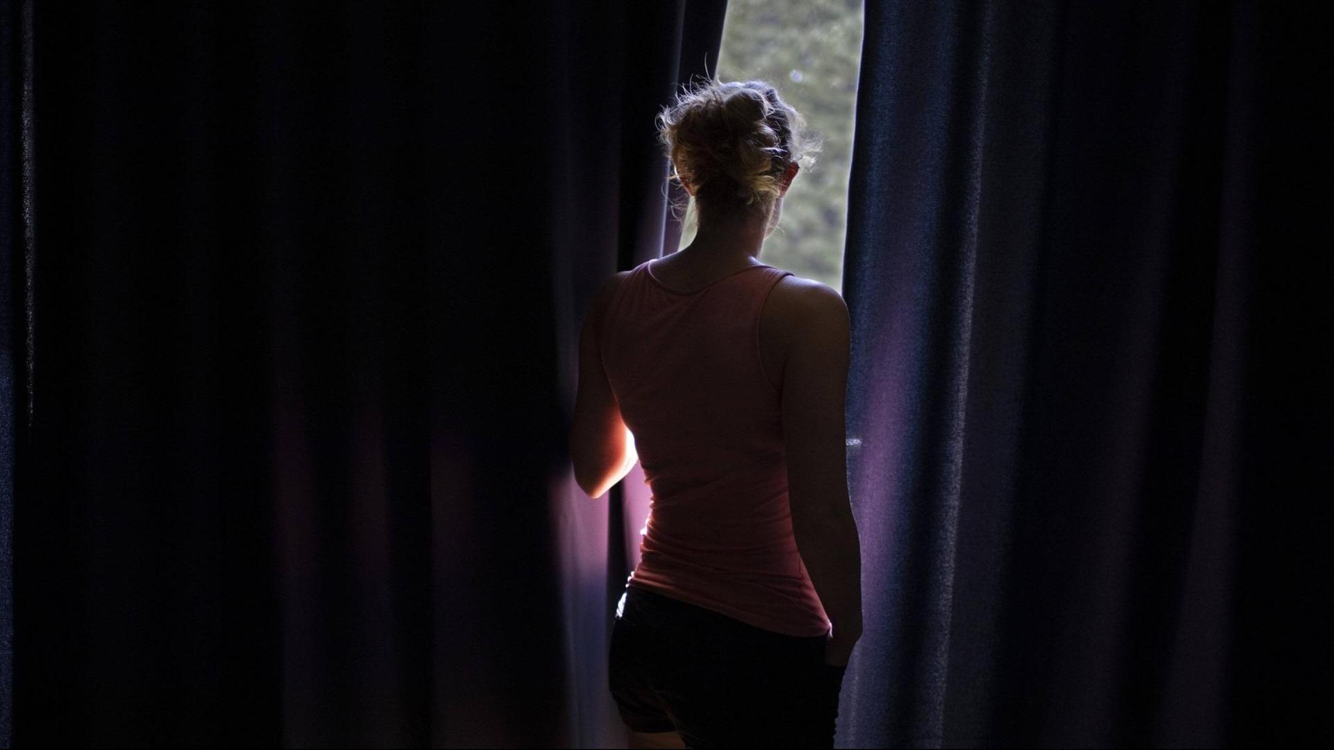 Eine Frau schaut zwischen dicken Vorhängen zum Fenster heraus. Eine Frau schaut zwischen dicken Vorhängen zum Fenster heraus.