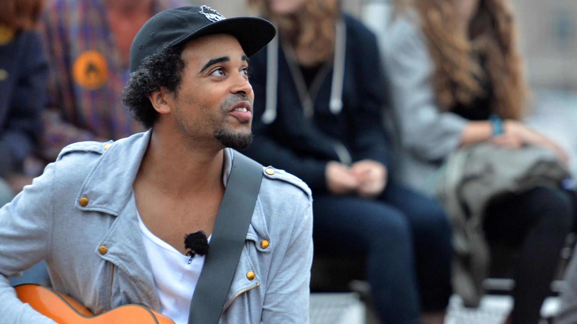 Patrice sitzt umgeben von Fans auf dem Badeschiff in Berlin. Er hält eine Gitarre in der Hand.