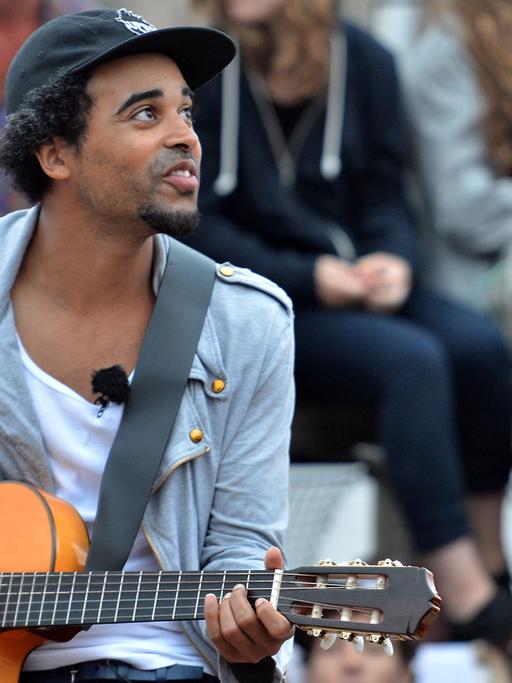 Patrice sitzt umgeben von Fans auf dem Badeschiff in Berlin. Er hält eine Gitarre in der Hand.